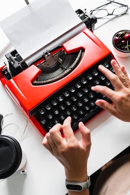 As mãos das mulheres estão digitando em uma máquina de escrever vintage vermelha brilhante