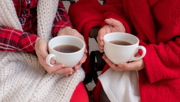 As mãos das mulheres estão segurando uma xícara branca de chá ou café, vestidas com roupas festivas vermelhas e brancas