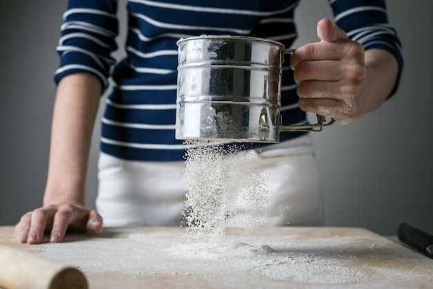 As mãos das mulheres polvilhe uma tábua de madeira com farinha branca para cozinhar. Farinha congelada dinamicamente em voo