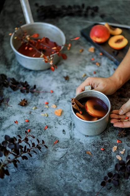 As mãos das mulheres seguram bagas e uma caneca rústica metálica com bebida quente não alcoólica caseira