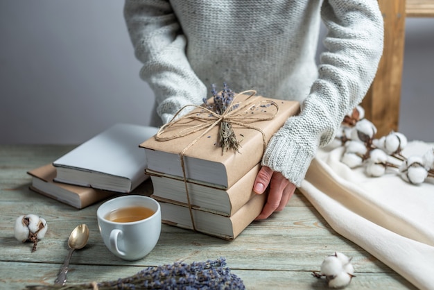 As mãos das mulheres seguram cuidadosamente uma pilha de livros em capas de papel artesanal, enroladas com corda e decoradas com alfazema