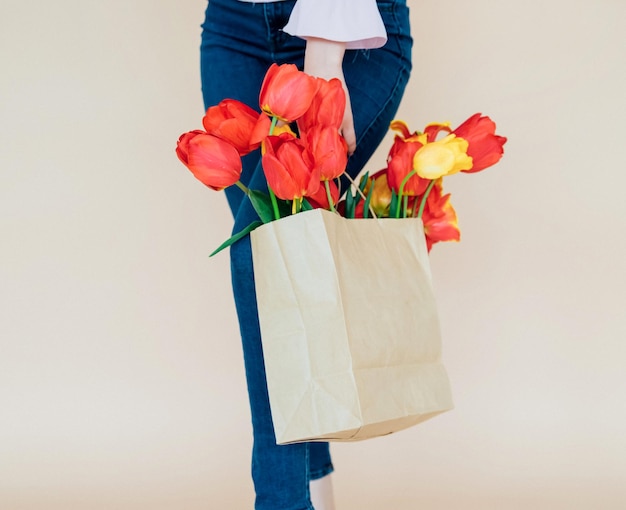 As mãos das mulheres seguram um buquê de tulipas vermelhas em um saco de papel em um fundo bege Dia dos Namorados Feliz Dia da Mulher Dia das Mães