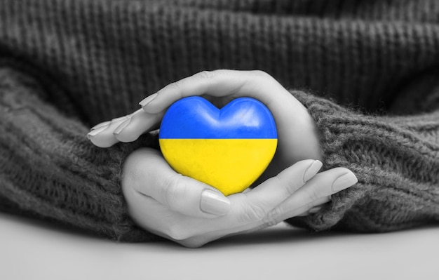 As mãos das mulheres seguram um coração nas cores da bandeira ucraniana rezam pela Ucrânia