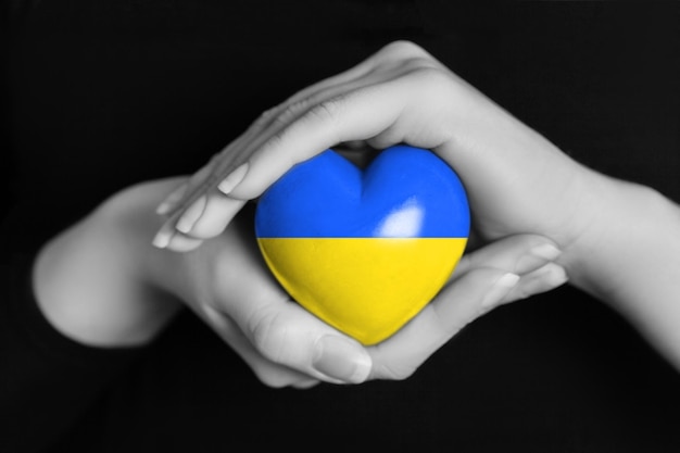 As mãos das mulheres seguram um coração nas cores da bandeira ucraniana rezem pela Ucrânia Fique com a Ucrânia
