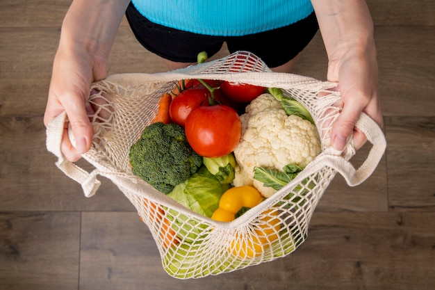 As mãos das mulheres seguram um saco com legumes frescos no fundo de um piso de madeira Vista superior plana