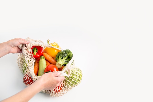 As mãos das mulheres tiram legumes frescos de um saco em uma mesa branca Vista superior plana