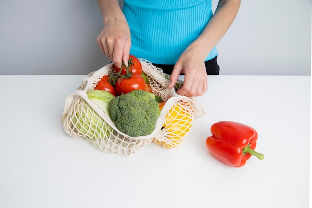 As mãos das mulheres tiram legumes frescos de um saco em uma mesa branca Vista superior plana