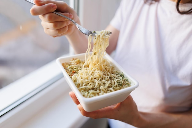 As mãos de alguém comendo uma refeição rápida de macarrão instantâneo capturadas em um close-up