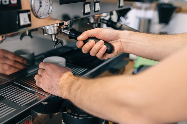 As mãos de um barista profissional segurando uma xícara branca na grelha da máquina de café