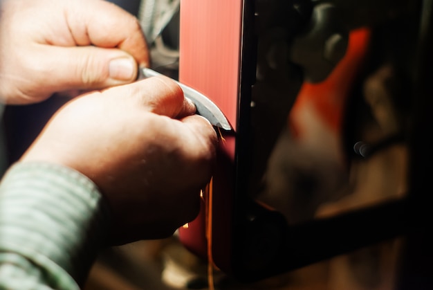 As mãos de um chaveiro afiando a peça de trabalho para uma faca em uma cinta de esmerilar