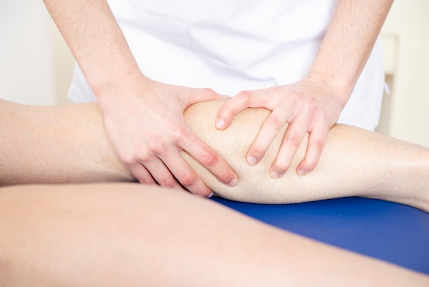 As mãos de um fisioterapeuta massageando a perna de um atleta.