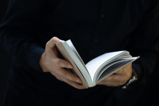 As mãos de um homem com roupas pretas que segura um livro e tenta abri-lo