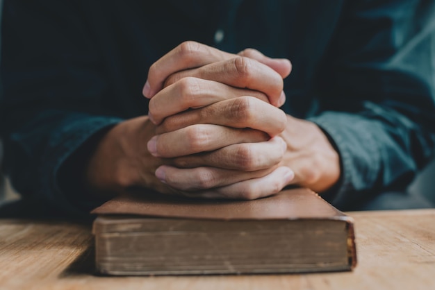 As mãos de um homem orando sobre uma Bíblia representam fé e espiritualidade na vida cotidiana. fechar-se.