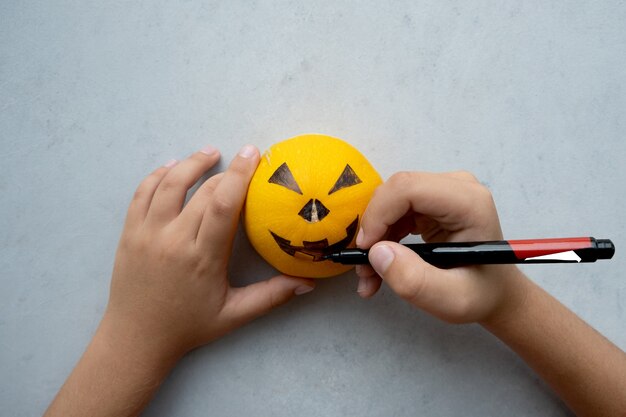 As mãos de um menino desenhando um focinho assustador em uma abóbora para o feriado de halloween. minimalismo. cinza e laranja.