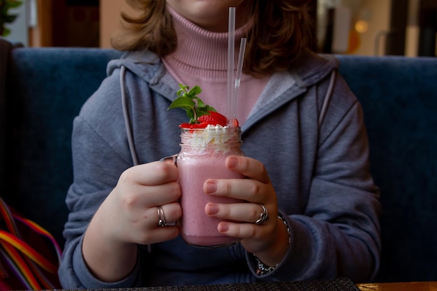 Foto as mãos de uma adolescente estão segurando um coquetel rosa leitoso, uma bebida deliciosa em um restaurante