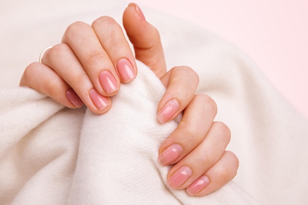 As mãos de uma garota com unhas bem cuidadas e desarrumadas e regeneradas com esmalte de gel e cobertas com g