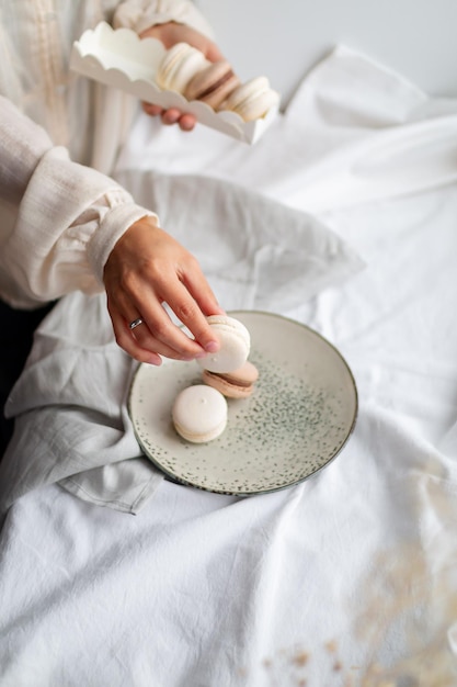 As mãos de uma garota se espalharam e embrulharam macarons franceses como presente na luz da manhã em cores pastel delicadas.