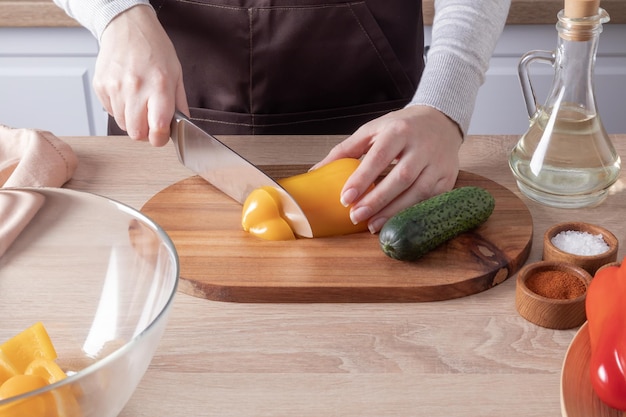 As mãos de uma jovem cortam uma salada de legumes em uma placa de madeira e um plano de curto prazo de bancada de cozinha