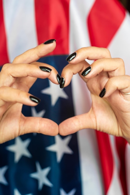 As mãos de uma mulher formam um coração com a bandeira americana atrás delas.