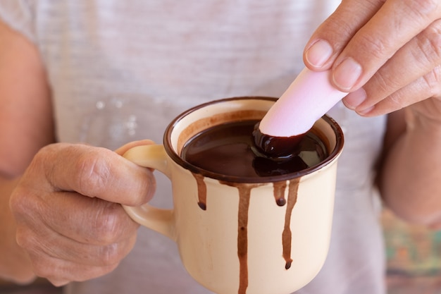 As mãos de uma mulher seguram uma xícara de chocolate quente enquanto colocam um marshmallow dentro