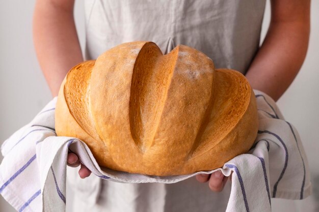 As mãos de uma mulher segurando um pão rústico recém-assado iluminado pelo sol da manhã o conceito de alimentação saudável em casa