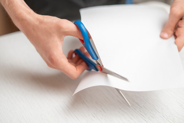 As mãos de uma pessoa segurando um pedaço de folha de papel e cortá-lo com uma tesoura