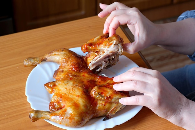 Foto as mãos de uma senhora idosa operam um frango grelhado e o exibem na cozinha em uma mesa marrom sem rosto fechado