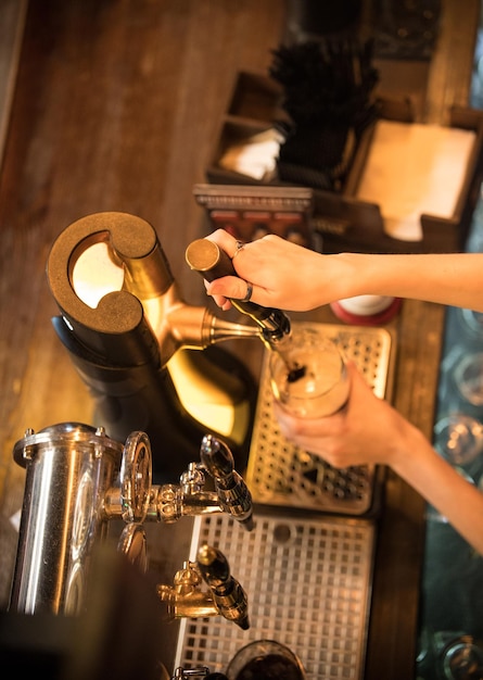 As mãos do barman derramam cerveja da torneira no copo