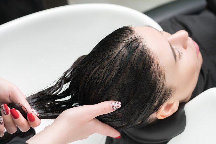 As mãos do cabeleireiro lavam os cabelos longos da mulher morena com shampoo em uma pia especial para lavar no salão de cabeleireiro.