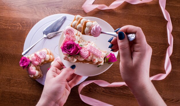 As mãos do confeiteiro com um delicado e delicioso bolo de letras. Bolo com flores vivas, chocolate branco, beas. Mãos de um chef de pastelaria, embalando a sobremesa.