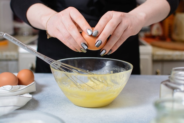 As mãos do cozinheiro seguram um ovo inteiro sobre uma tigela de vidro com massa