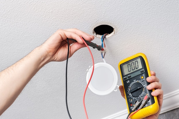 As mãos do eletricista verificam a fonte de alimentação do testador antes de instalar a luz LED