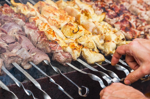 As mãos do homem estão fritando um shish kebab na grelha Frango de porco e carne de cordeiro em espetos no gri