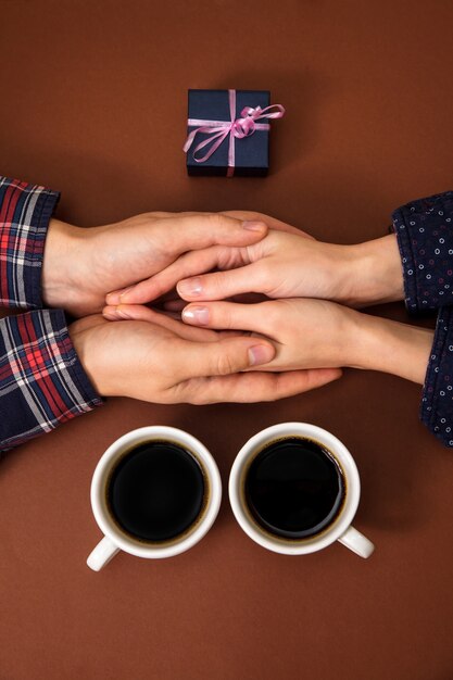 As mãos do homem mantêm as mãos da mulher perto de presente e duas xícaras de café em marrom.