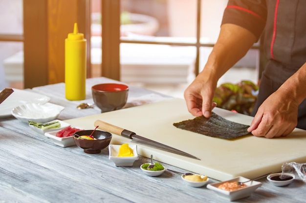 As mãos do homem tocam a folha de nori. Nori na placa de cozinha. Ingrediente básico para rolos de sushi. Manhã na cozinha do café.