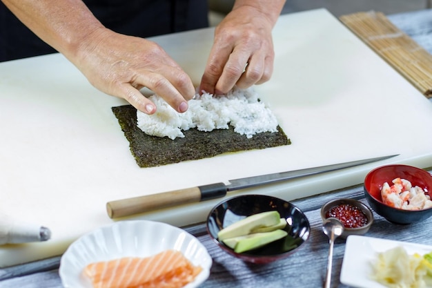 As mãos do homem tocam o arroz. Faca perto da tigela com abacate. Enchimento para rolos de uramaki. Chef de sushi habilidoso no trabalho.