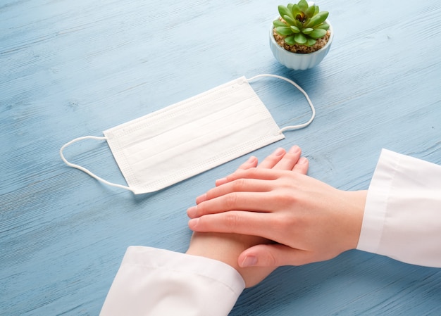 As mãos do médico com uma máscara médica na mesa.