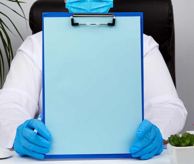 Foto as mãos do médico feminino em luvas de látex médicas azuis detém uma pasta com um clipe de papel