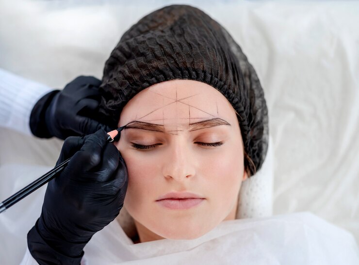 Foto as mãos do mestre de maquiagem permanente desenham uma nova forma de sobrancelhas para a garota modelo usando lápis profissional. retrato de close up