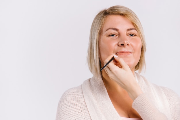 As mãos do mestre delineiam os lábios com um lápis para uma mulher adulta. conceito de maquiagem e beleza em fundo branco. foto de alta qualidade