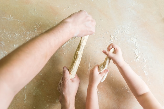 As mãos do pai e da criança criam massa crua