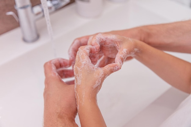 as mãos do pai e da criança dobraram a espuma de sabão em forma de coração com bolhas cobrindo as palmas das mãos