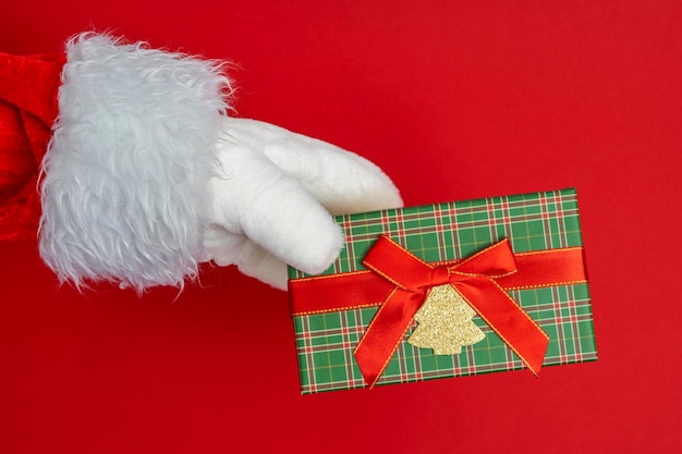 As mãos do Papai Noel estão segurando um presente para o fundo vermelho de Natal