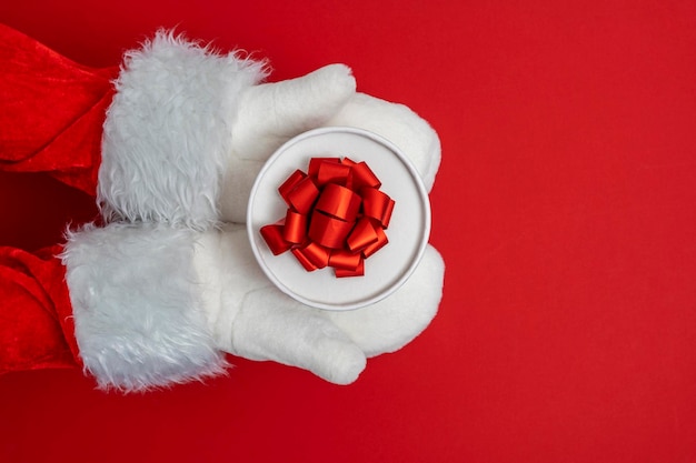 As mãos do Papai Noel estão segurando um presente para o fundo vermelho de Natal
