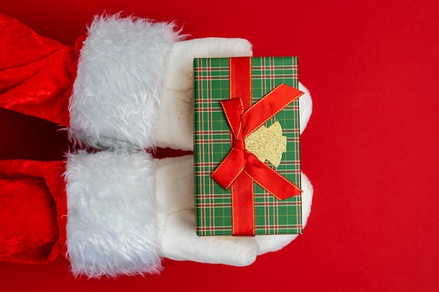 As mãos do Papai Noel estão segurando um presente para o fundo vermelho de Natal