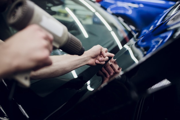 Foto as mãos do trabalhador instalam capô de filme plástico de proteção de pintura de carro