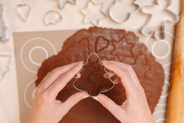 As mãos dos chefs de confeitaria seguram a forma de metal de abeto preparando massa para assar pão de gengibre.