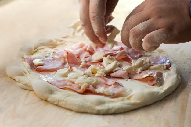 As mãos dos cozinheiros espalham presunto e queijo na massa de pizza.