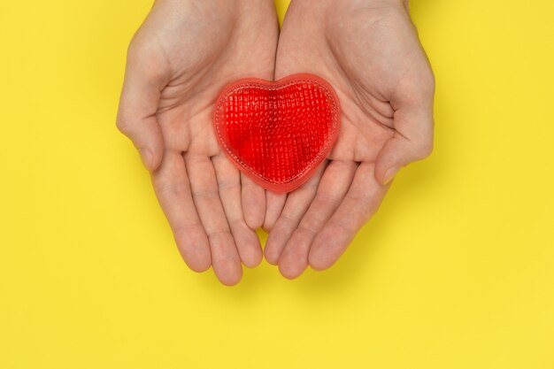 As mãos dos homens estão segurando um coração vermelho em uma parede amarela. amor, conceito de relacionamento.