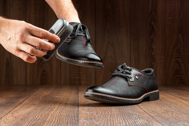 As mãos dos homens limpam sapatos pretos em uma parede de madeira. O conceito de engraxate, cuidados com a roupa, serviços.